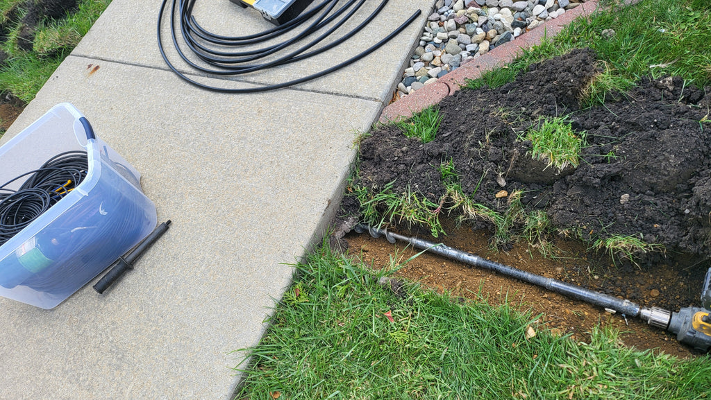 Hose on a sidewalk next to a garden bed with soil and grass.